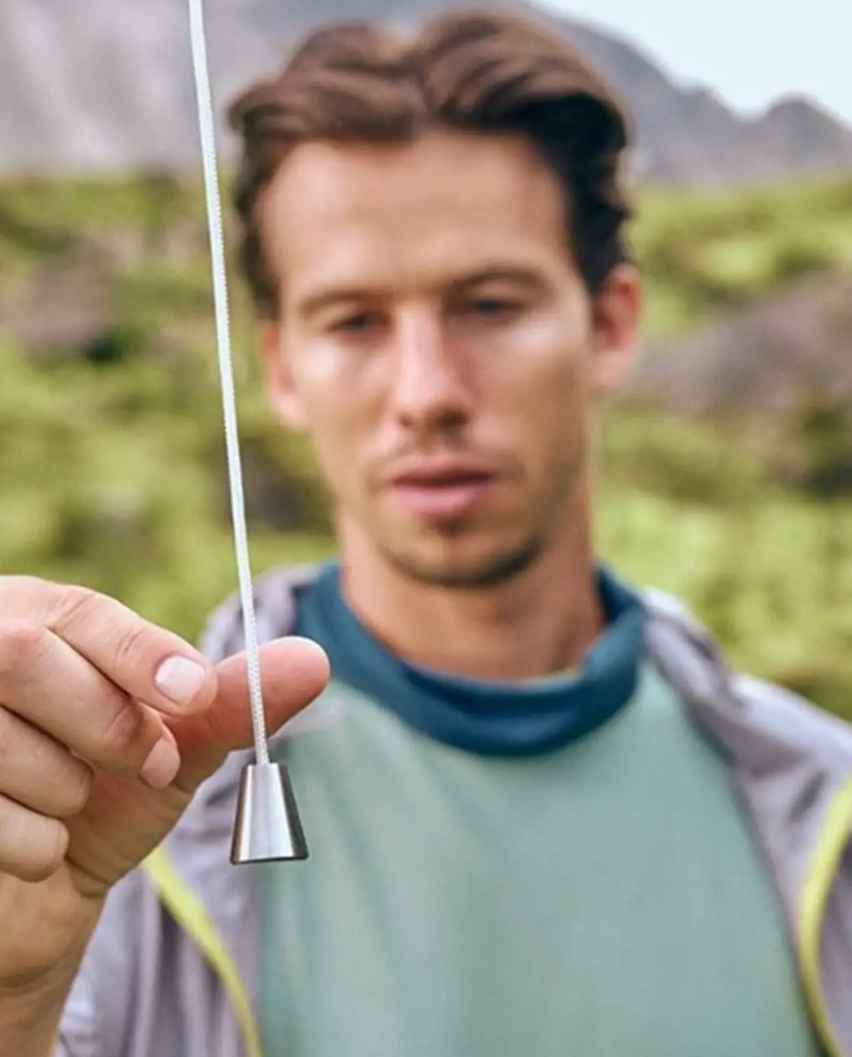 A young man in sports attire stands in an alpine landscape and pulls a string that hangs from the sky.