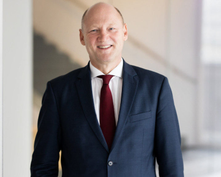 Achim Kaspar smiles into the camera. He is wearing a white shirt, a bordeau-coloured tie and a dark blue suit.